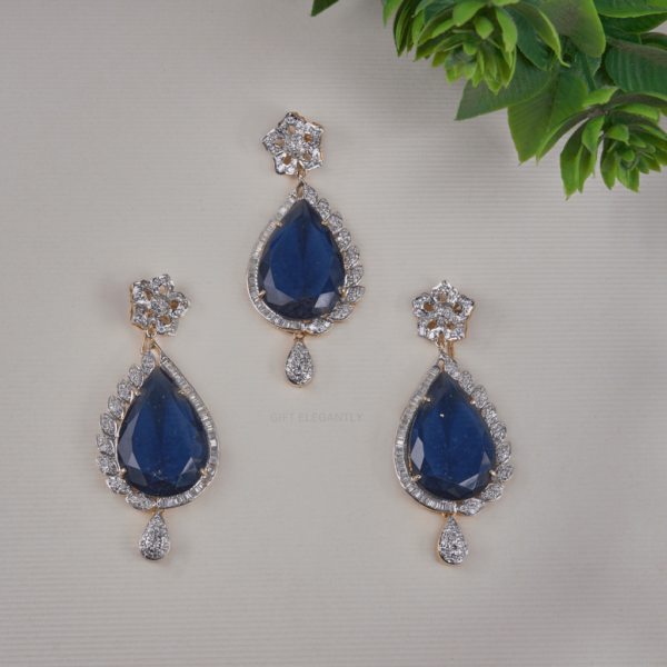 The Serenity Drop Pendant Set by Gift Elegantly features a large pear-shaped blue stone, accented by baguette and round diamonds for a captivating look. Perfect for special occasions