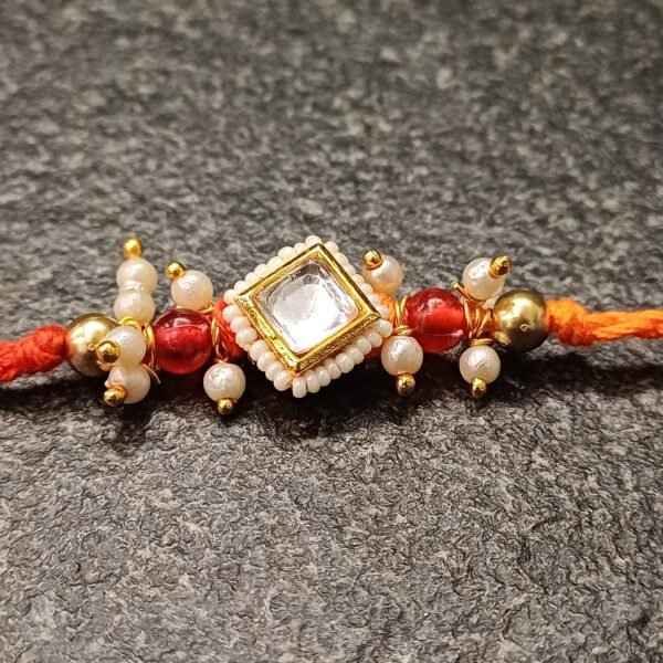 Square kundan rakhi with pearls and red beads on orange thread